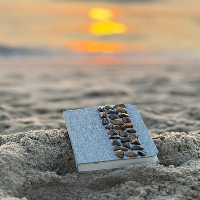 Liniertes Notizbuch (14 x 10 cm) mit echten Tigerauge-Steinen, energetisiert mit REIKI-Energie; fördert Intuition, Schutz, Klarheit und Selbstvertrauen. Jedes Notizbuch ist einzigartig durch individuelle Steinmuster und spirituelle Aufladung.