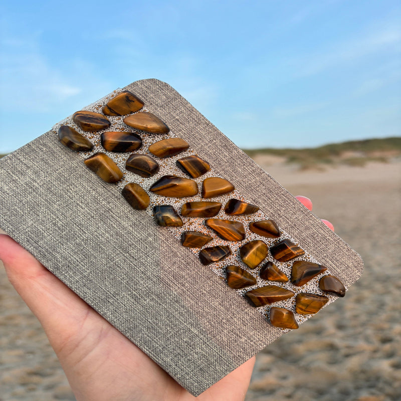 Liniertes Notizbuch (14 x 10 cm) mit echten Tigerauge-Steinen, energetisiert mit REIKI-Energie; fördert Intuition, Schutz, Klarheit und Selbstvertrauen. Jedes Notizbuch ist einzigartig durch individuelle Steinmuster und spirituelle Aufladung.